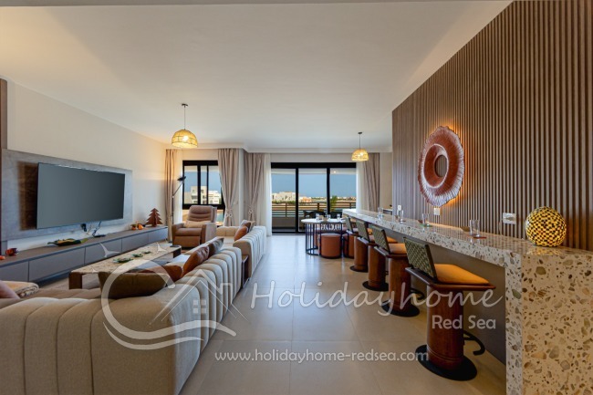 Tastefully furnished living room with a large Smart TV, bar, dining table, and balcony